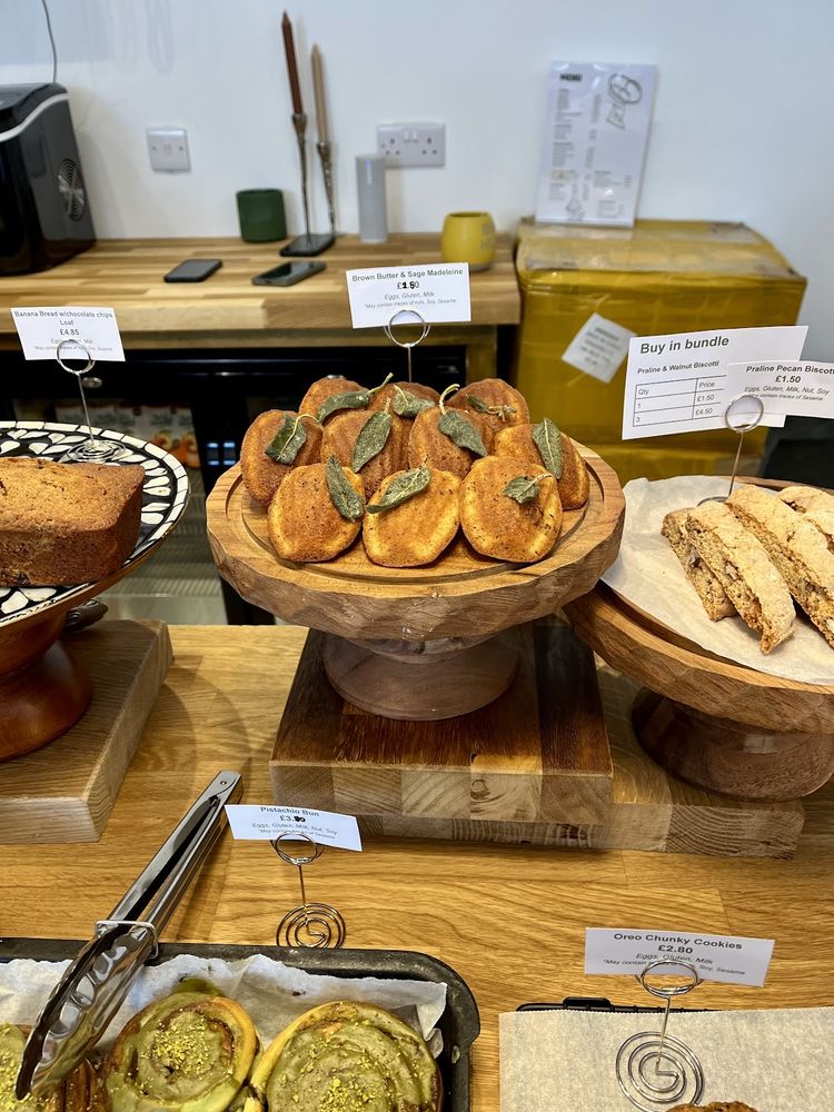 The bakery counter display of pistachio-topped buns on a wooden riser, with biscotti and a cake