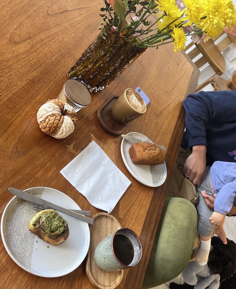 A table set with a pistachio pastry, a bun, coffees and a vase of yellow flowers